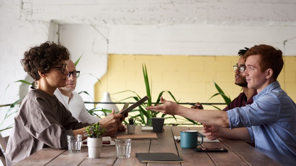 A team around a meeting table with mugs of coffee, mid-discussion